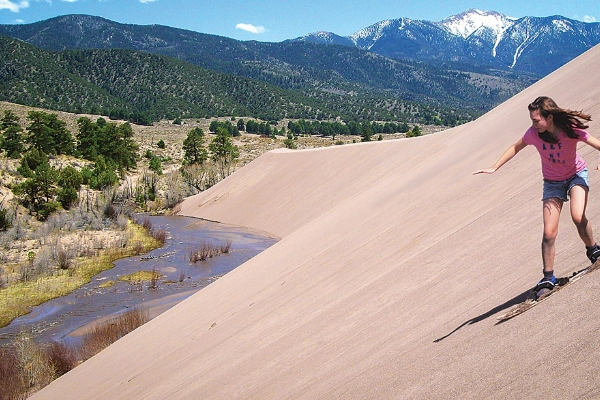 A person sandboarding down a steep sand dune