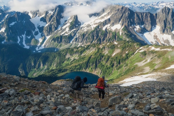 A hiker on a trail through alpine meadows with a massive glacier in the background