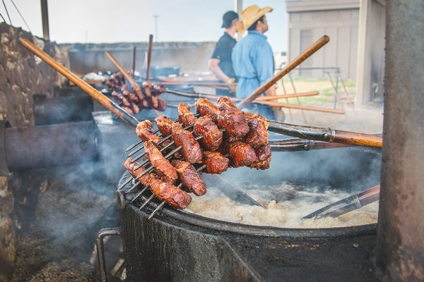 Steak being cooked on a pitchfork over an open flame with a badlands backdrop