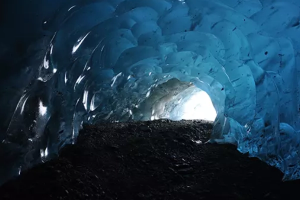 A hiker with crampons exploring a sparkling ice cave on a massive glacier