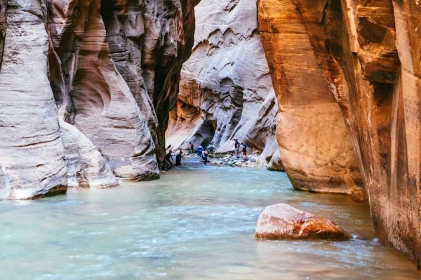 Hikers wading through a river at the bottom of a towering, narrow slot canyon